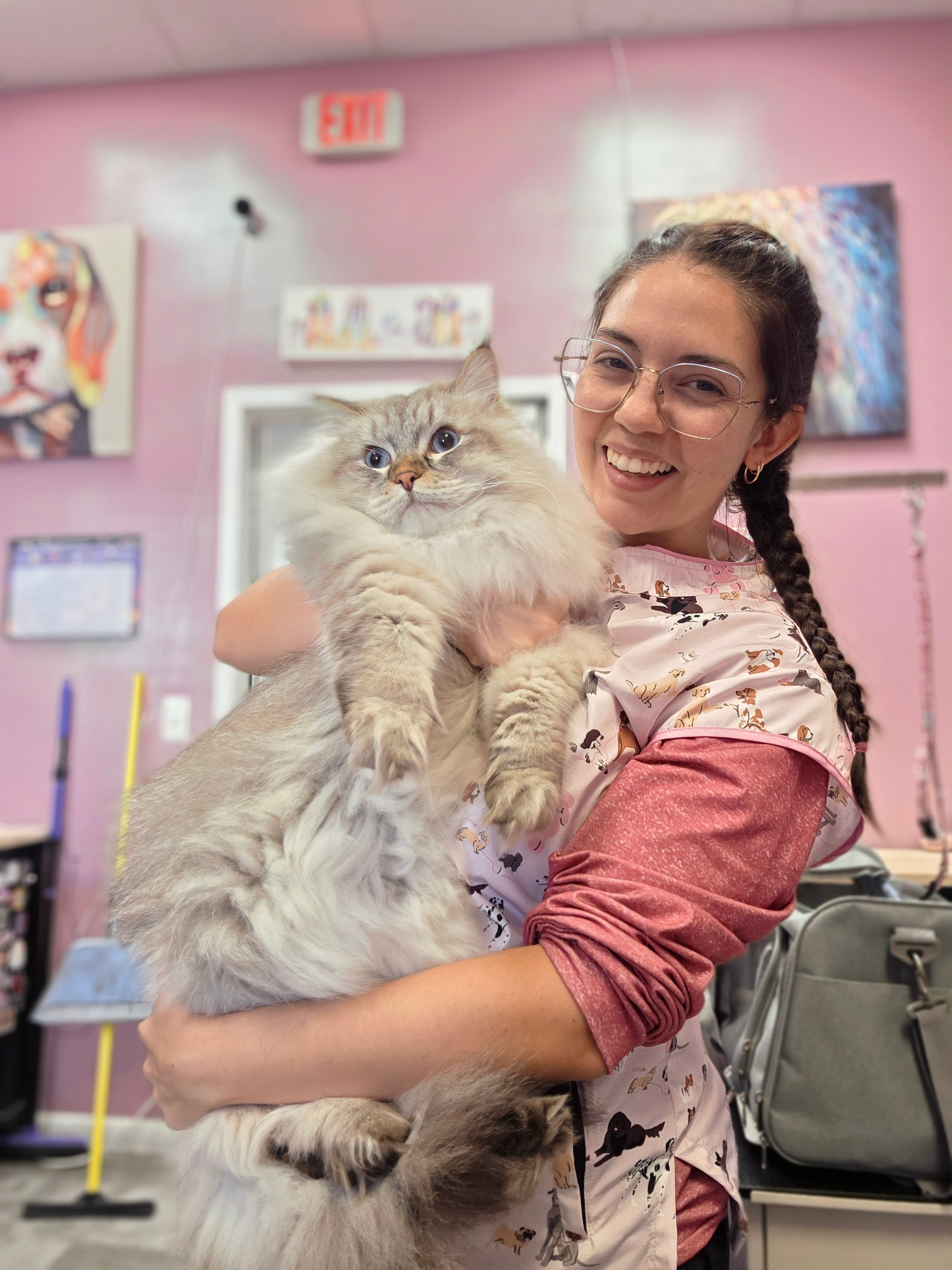 A smiling groomer holding a fluffy Persian cat at Little Jenna's Grooming salon